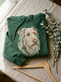 Gefalteter gruener Hoodie mit Line-Art-Portrait auf der Brust